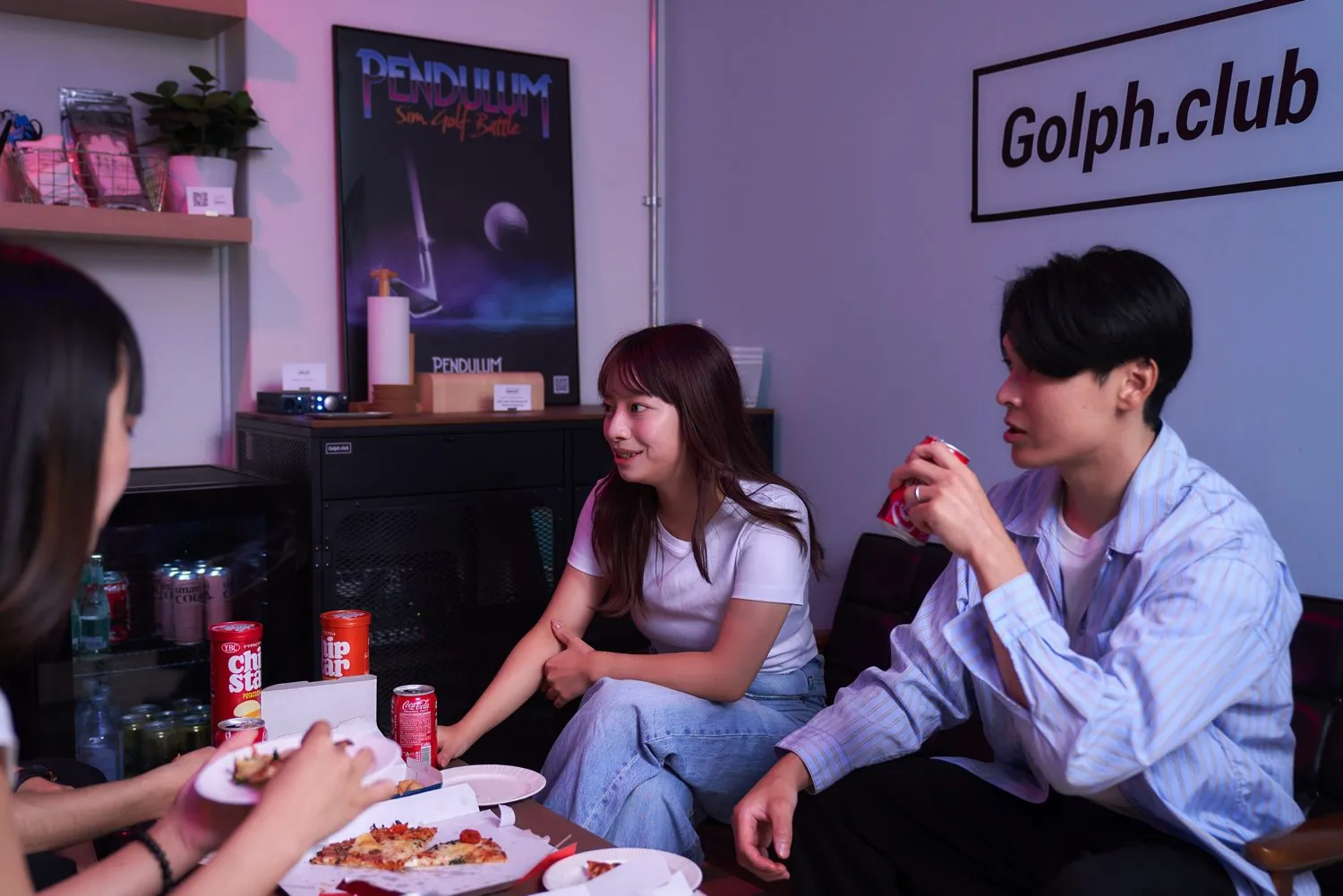 Golph.club の看板の下、ソファで仲間とピザを囲む